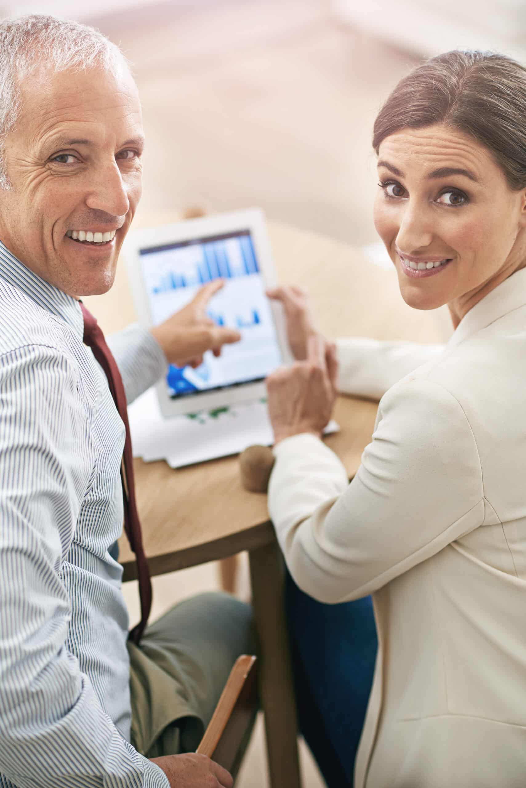 Portrait of two coworkers sitting at a table using a digital tablet.